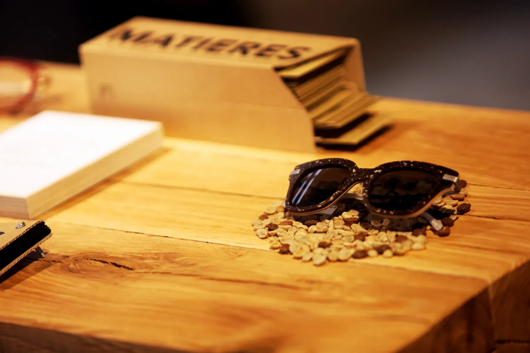 Lunettes de soleil posées sur un établi en bois, échantillons de matières et présentoir « Matières » en arrière-plan