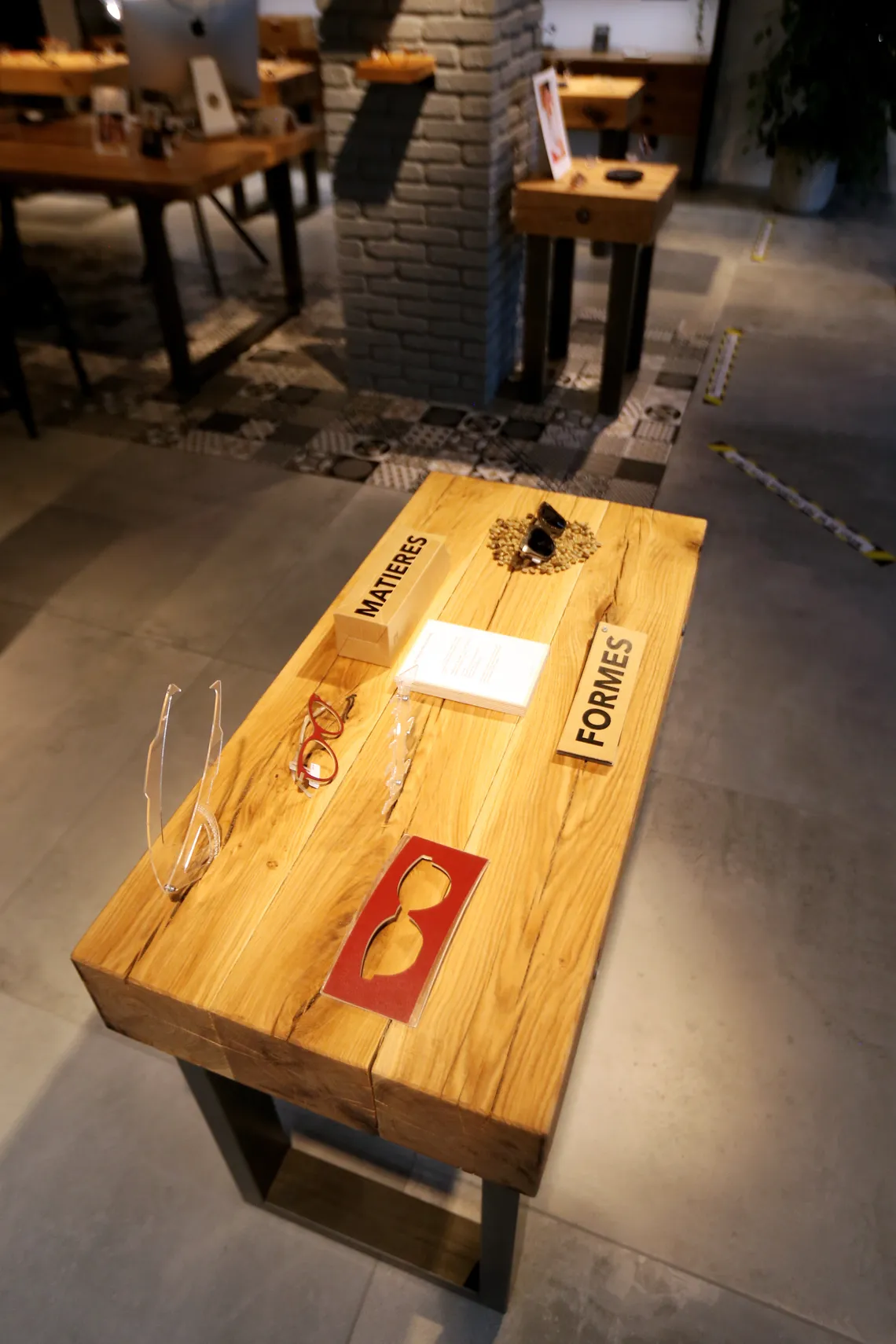 Table de présentation en bois de la boutique, avec les repères « Matières » et « Formes » et une sélection de montures
