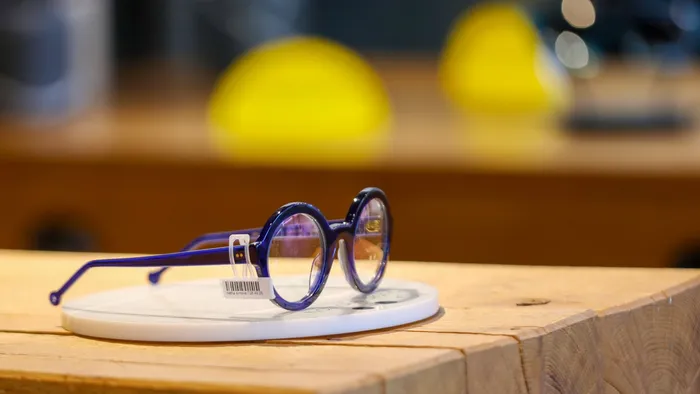 Une monture ronde bleu translucide est présentée sur un support blanc posé sur un comptoir en bois.