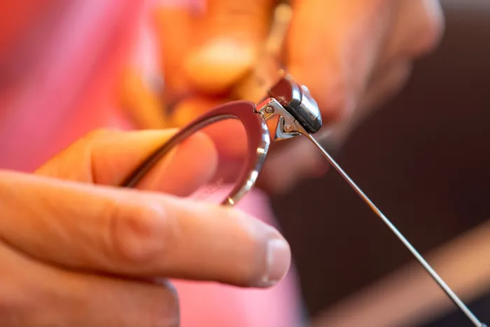 Ajustage du tenon d'une monture à la pince, gros plan sur les mains de l'opticien