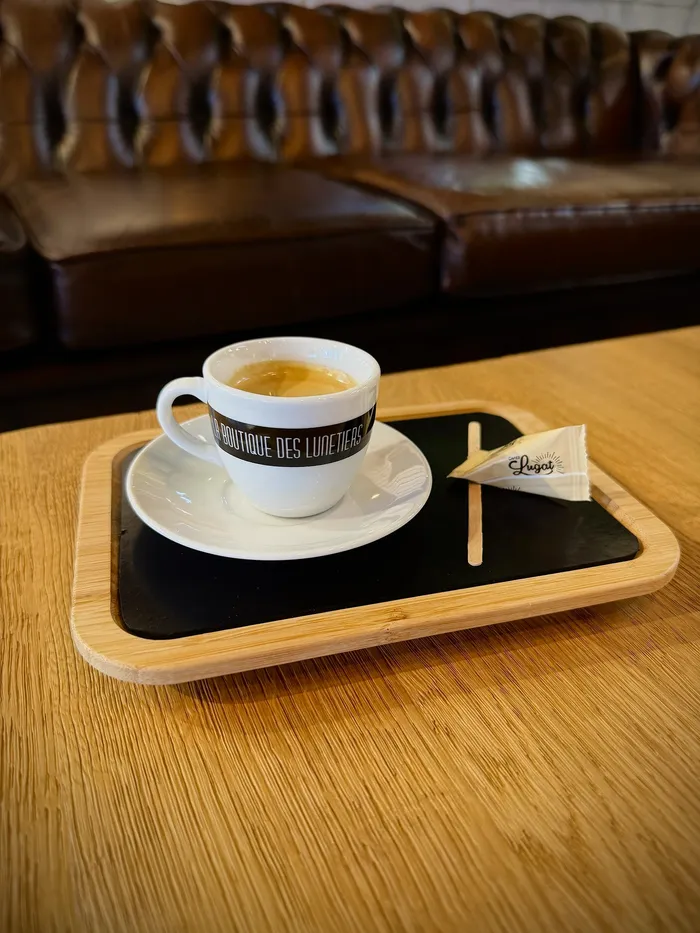 Tasse d'expresso « La Boutique des Lunetiers » servie sur un plateau, devant le canapé en cuir de la boutique