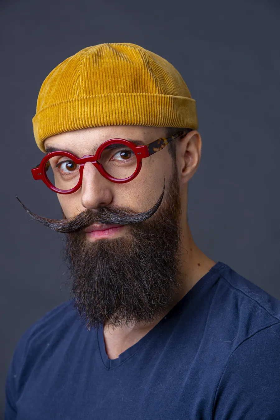 Portrait d'un homme barbu coiffé d'un bonnet jaune moutarde, portant une monture ronde en acétate rouge de La Brique et la Violette