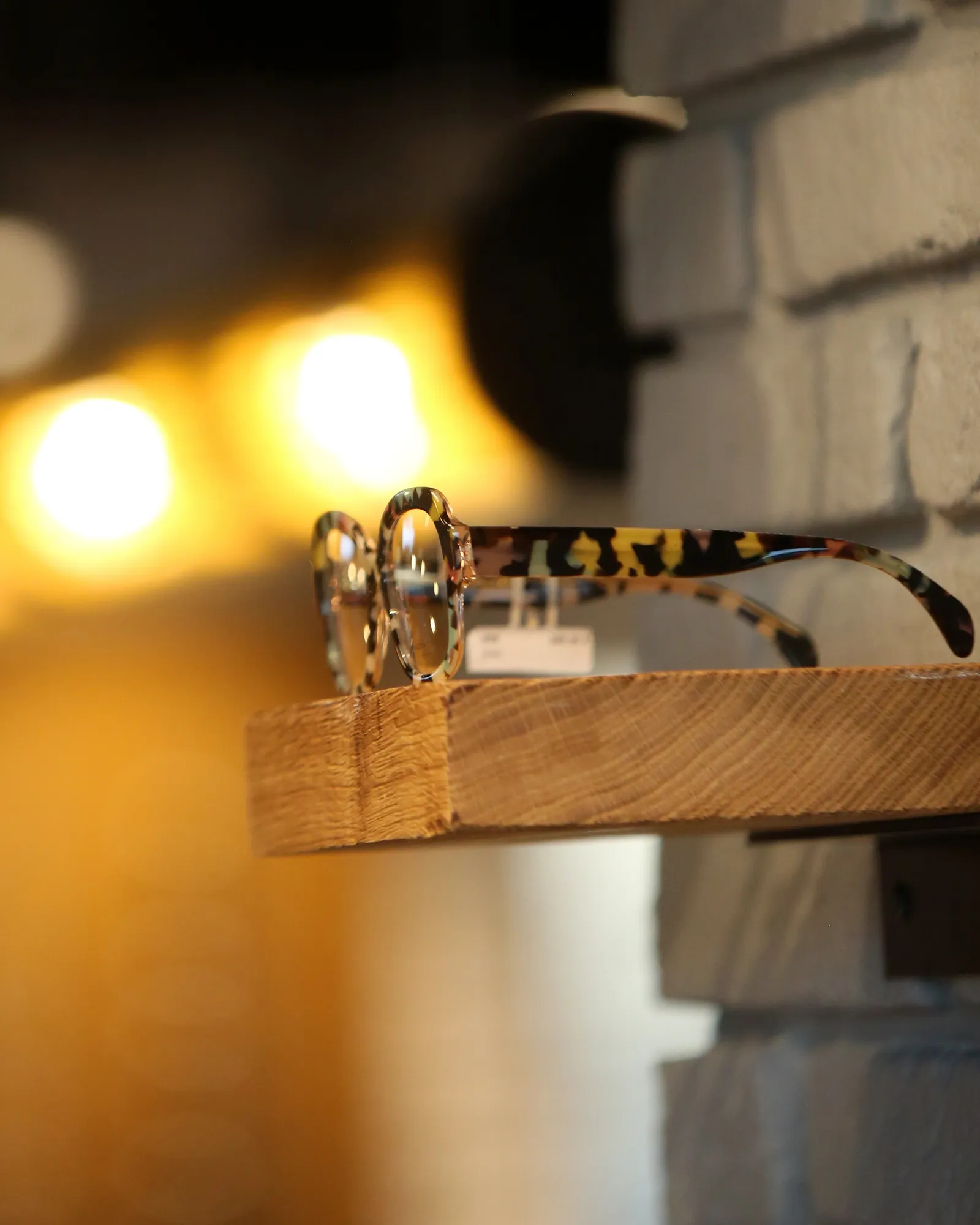 Monture optique ronde en acétate translucide marbré, branches écaille, posée sur une tablette en bois sous une lampe d'atelier, à La Boutique des Lunetiers