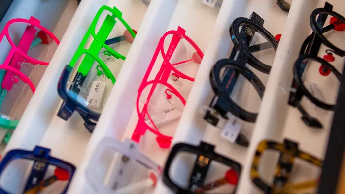 Un tiroir de présentation contient de nombreuses montures de lunettes colorées, rangées en lignes.