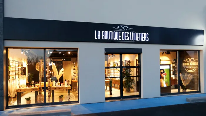 Vue extérieure de la façade éclairée de La Boutique des Lunetiers, avec vitrines et entrée centrale.