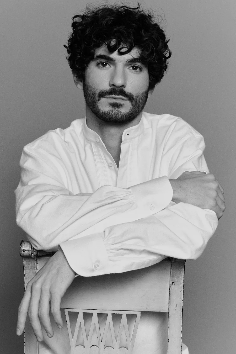 Portrait de Hermes Pontet, fondateur et designer de Pontet Eyewear, en noir et blanc, bras croisés sur le dossier d’une chaise